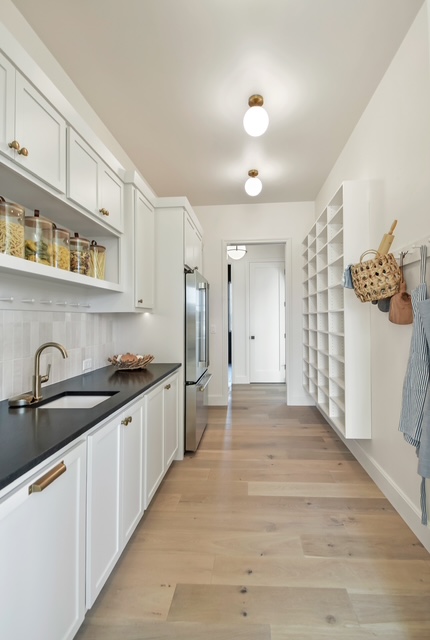 Custom kitchen with white cabinetry, open pantry shelving, and black countertops in Green Bay, WI.