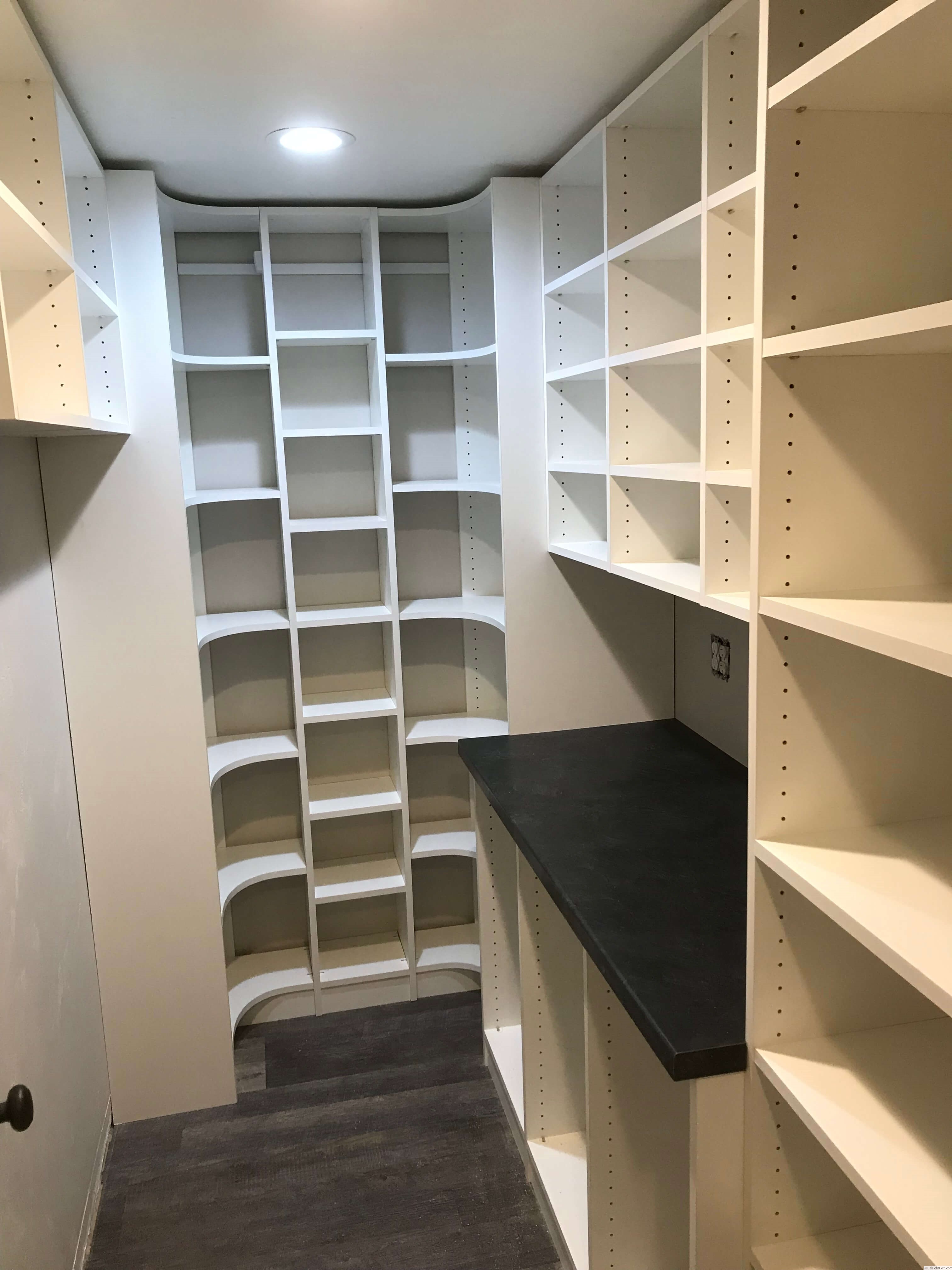 Custom pantry with curved shelving, built-in counter, and white storage units in Green Bay, WI.