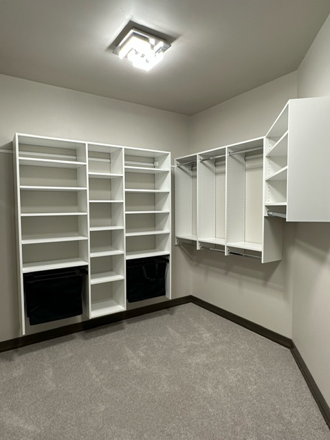 Custom walk-in closet with white open shelving, hanging space, and built-in black pull-out hampers in Green Bay, WI.