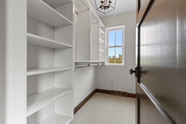 Custom walk-in closet with white shelving, hanging rods, and natural light from window in Green Bay, WI.