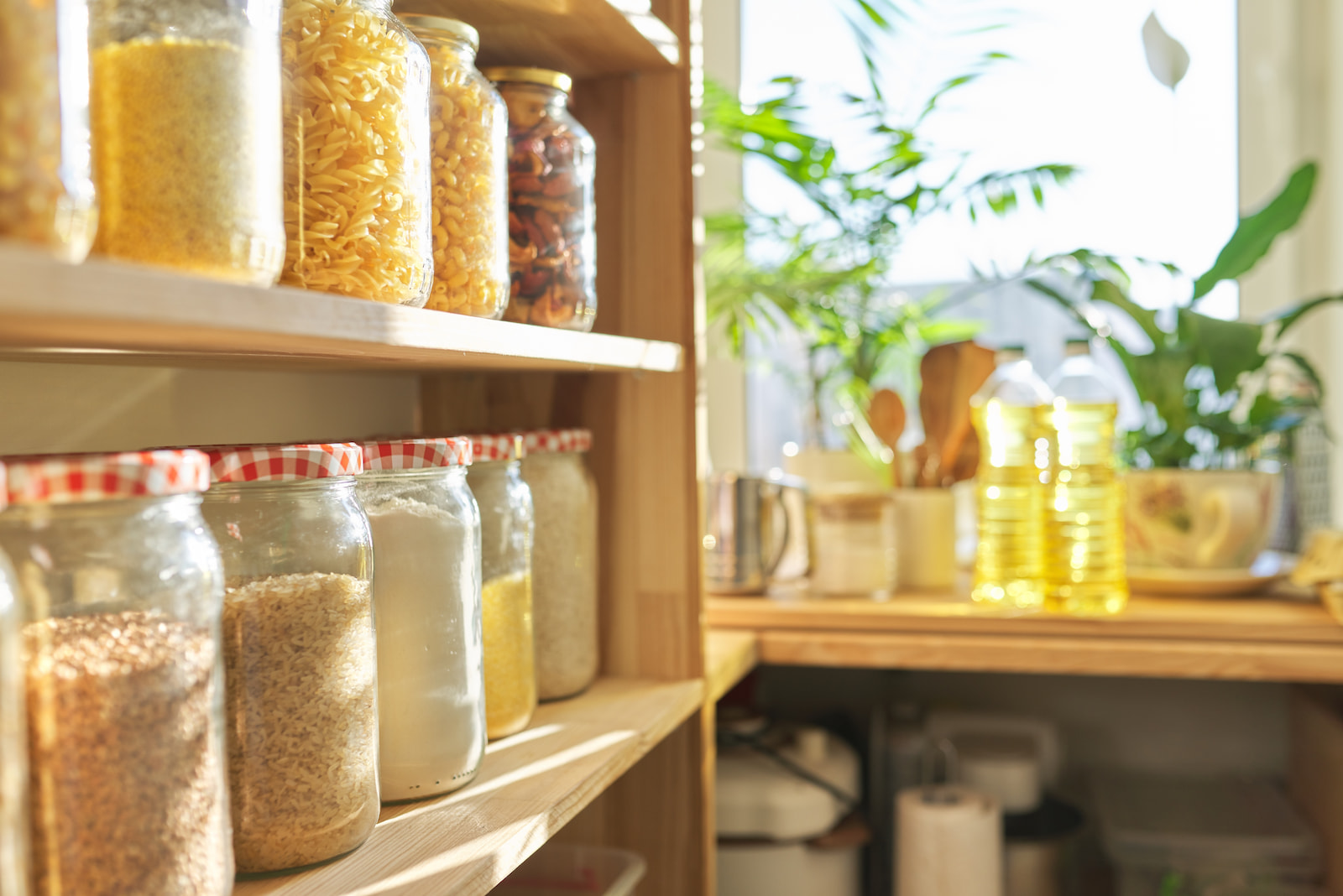 Pantry shelves with dry goods stored in glass jars and natural light streaming through nearby window.