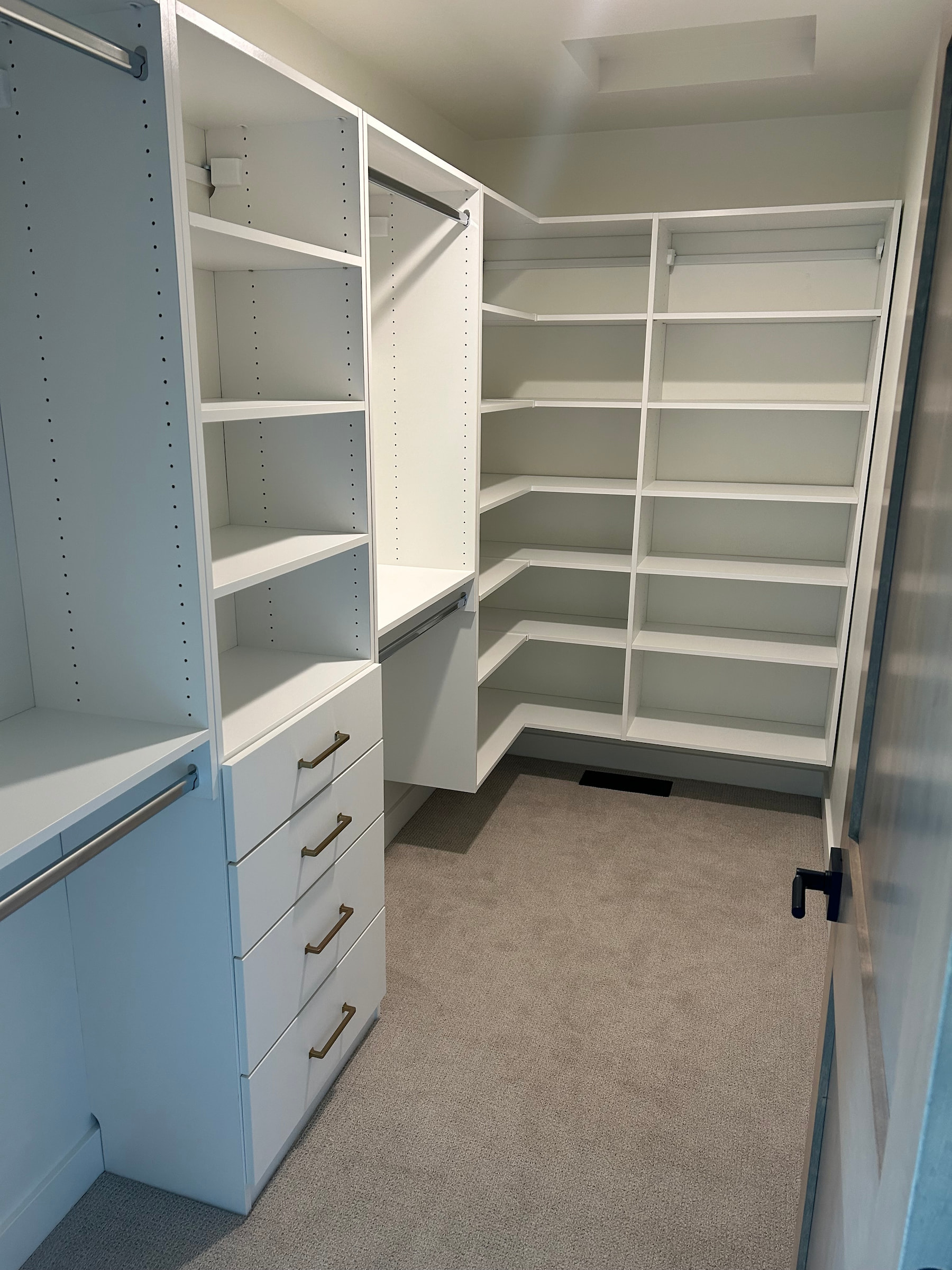 Spacious walk-in closet with white cabinetry, carpeted floor, and corner shelving.