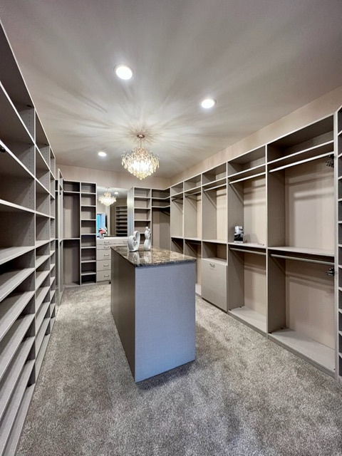 Luxury custom closet with center island, chandelier lighting, open shelving, and hanging storage in Green Bay, WI.