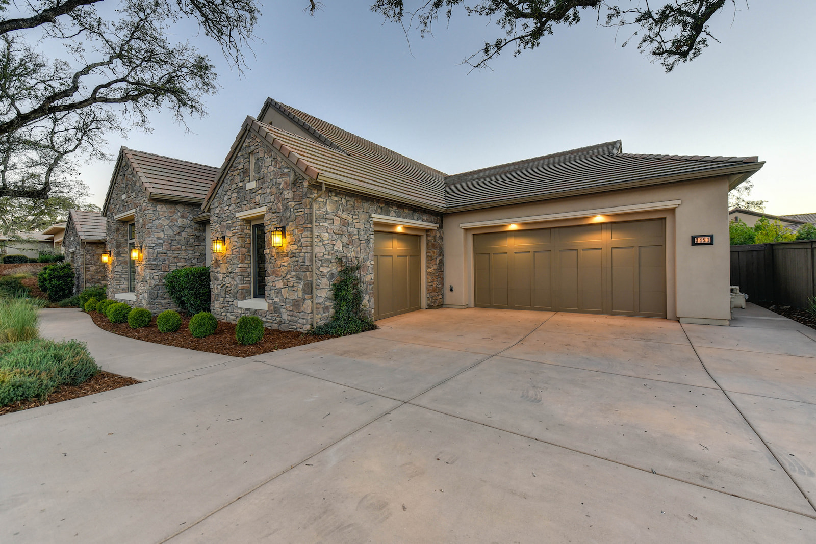 Custom home with stone exterior, three-car garage, and landscaped driveway at dusk.