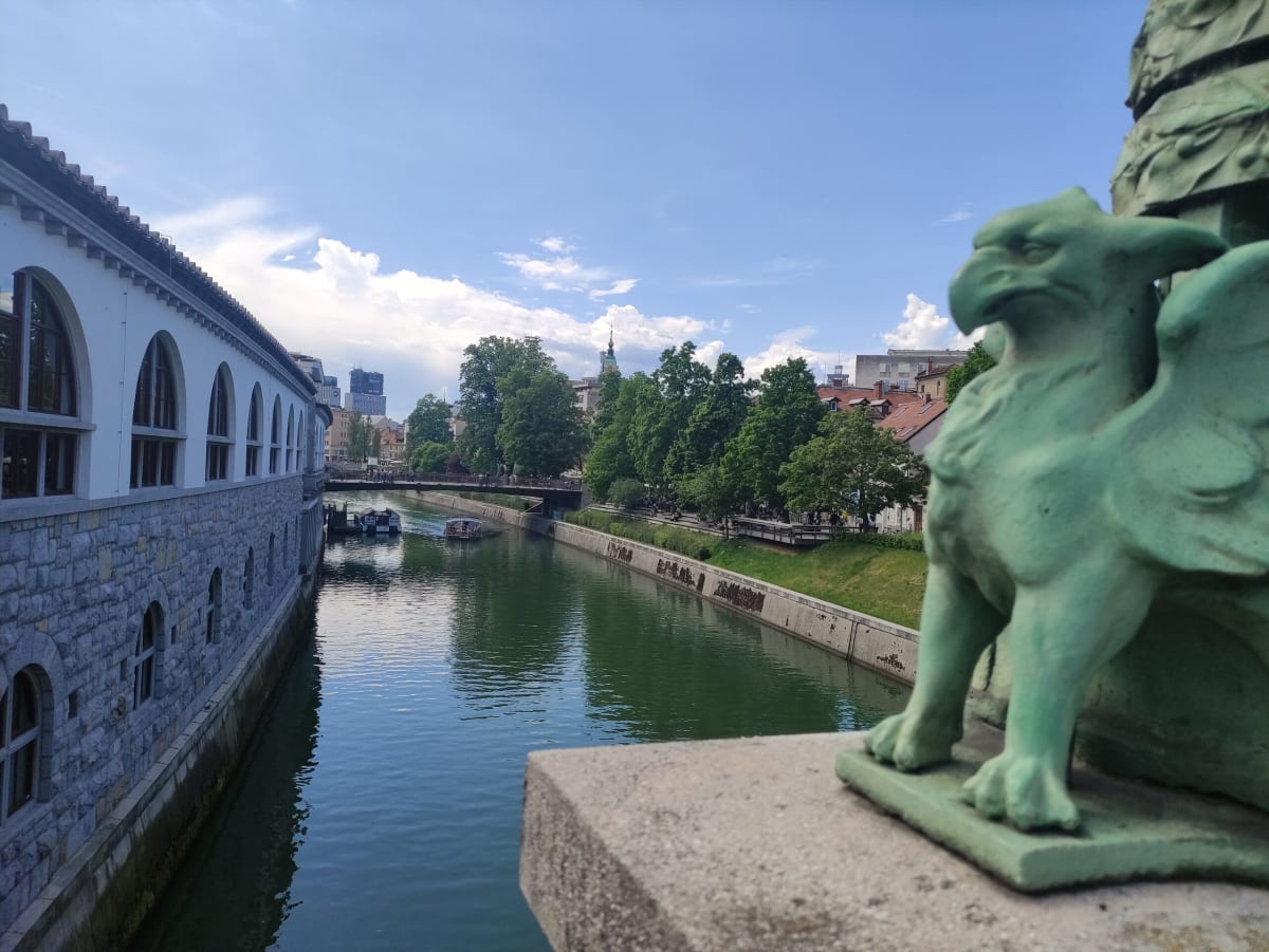 The Ljubljanica river through central Ljubljana seen from the Dragon Bridge, the long arcaded Central Market building on the left bank, a small tour boat on the water
