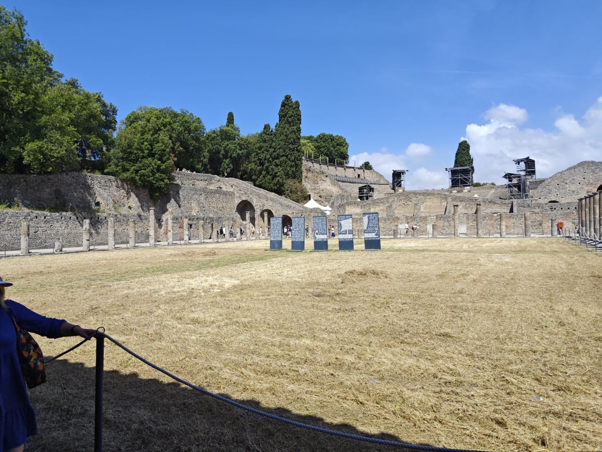 The palaestra of Pompeii's Quadriporticus — a huge dry-grass courtyard ringed by a stone colonnade under a bright summer sky