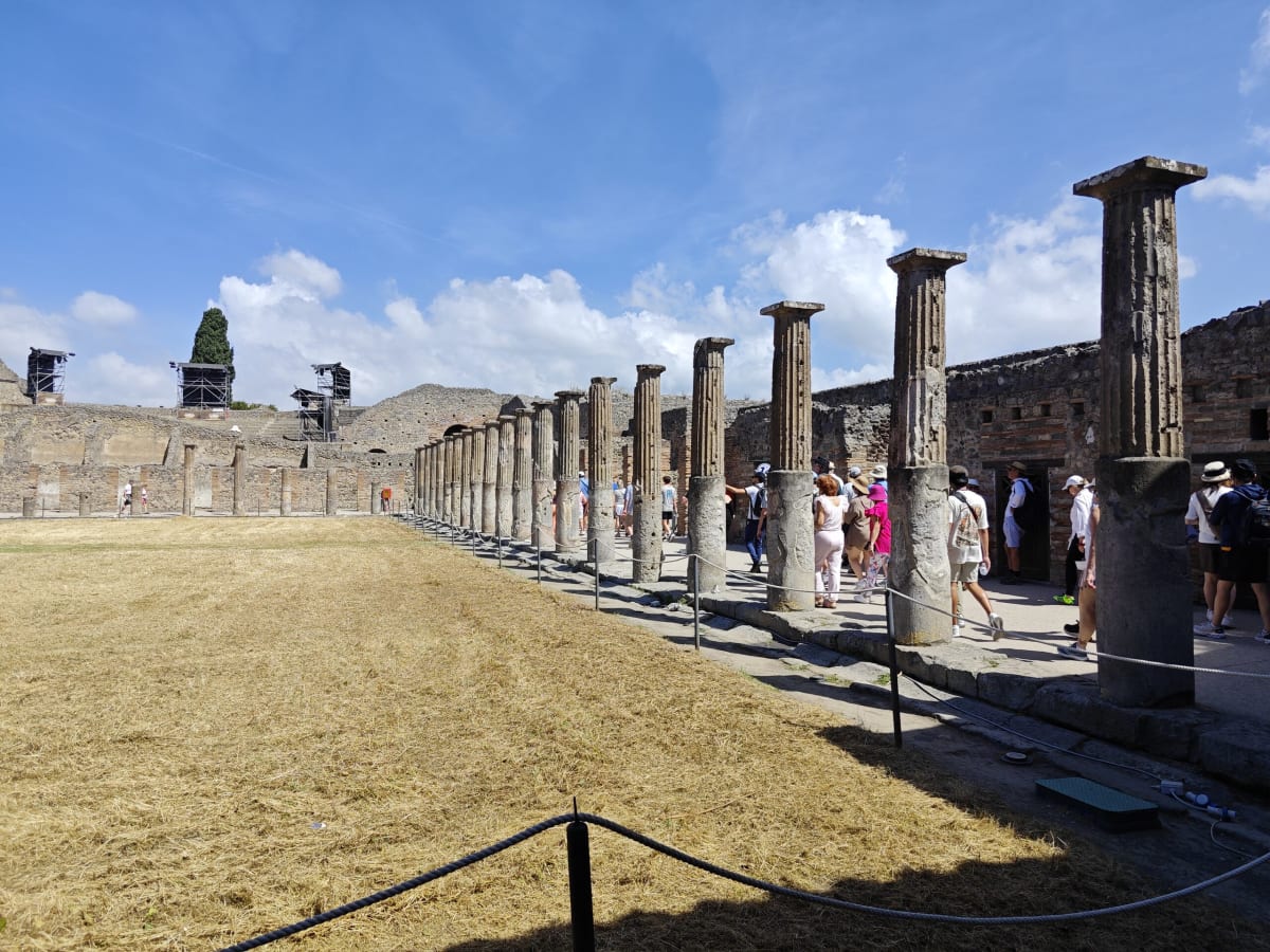 The colonnade of tall fluted columns along the edge of the same Pompeii courtyard, visitors walking in its shade