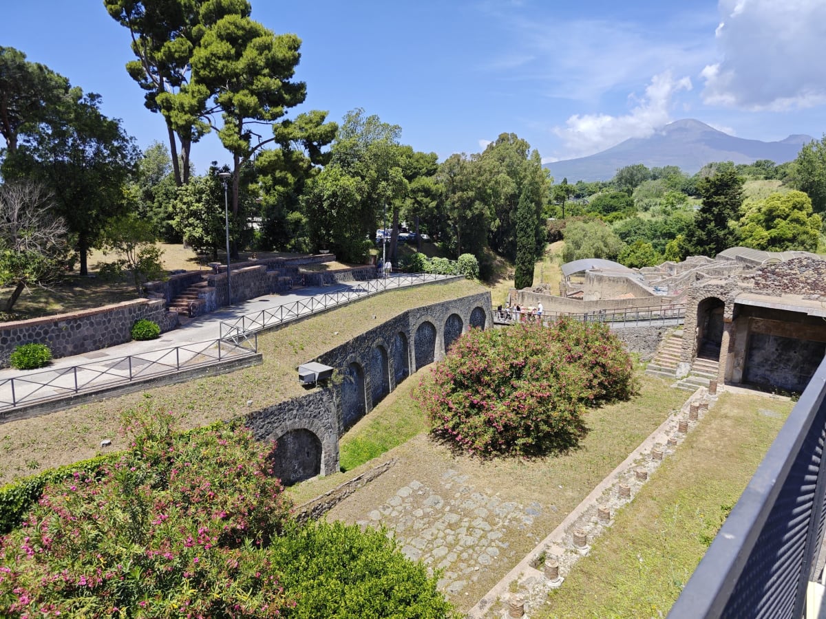 A terraced garden of pines and oleanders along an old arcaded wall inside the excavations, Vesuvius hazy in the distance