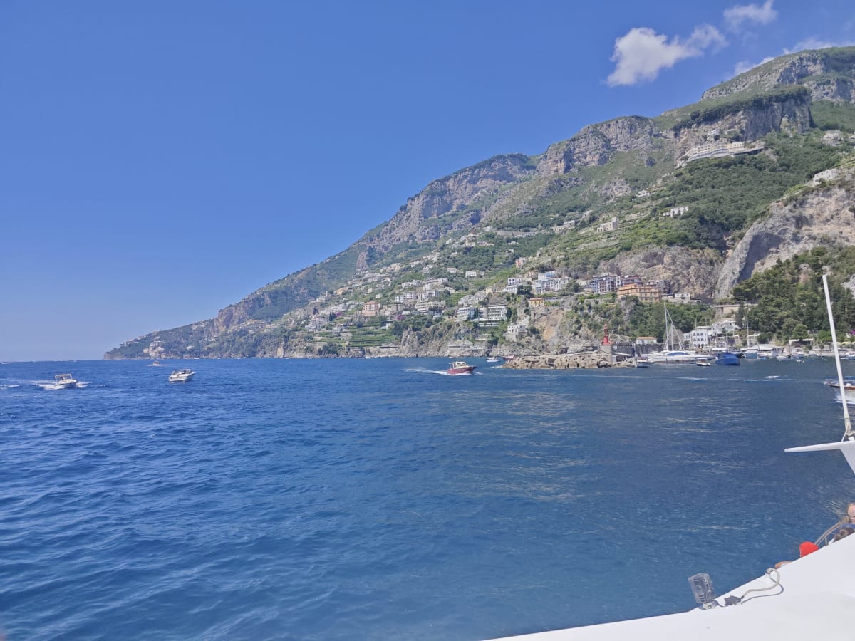 The Amalfi Coast seen from a boat, steep green mountains dropping to deep-blue water with boats and white villages along the foot