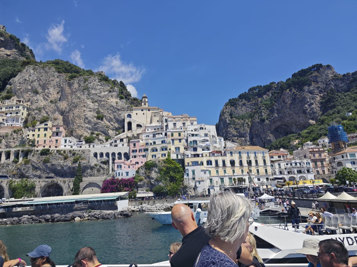A closer view of Amalfi's harbour front from the ferry, a promenade, terraces and bright bougainvillea against the cliff