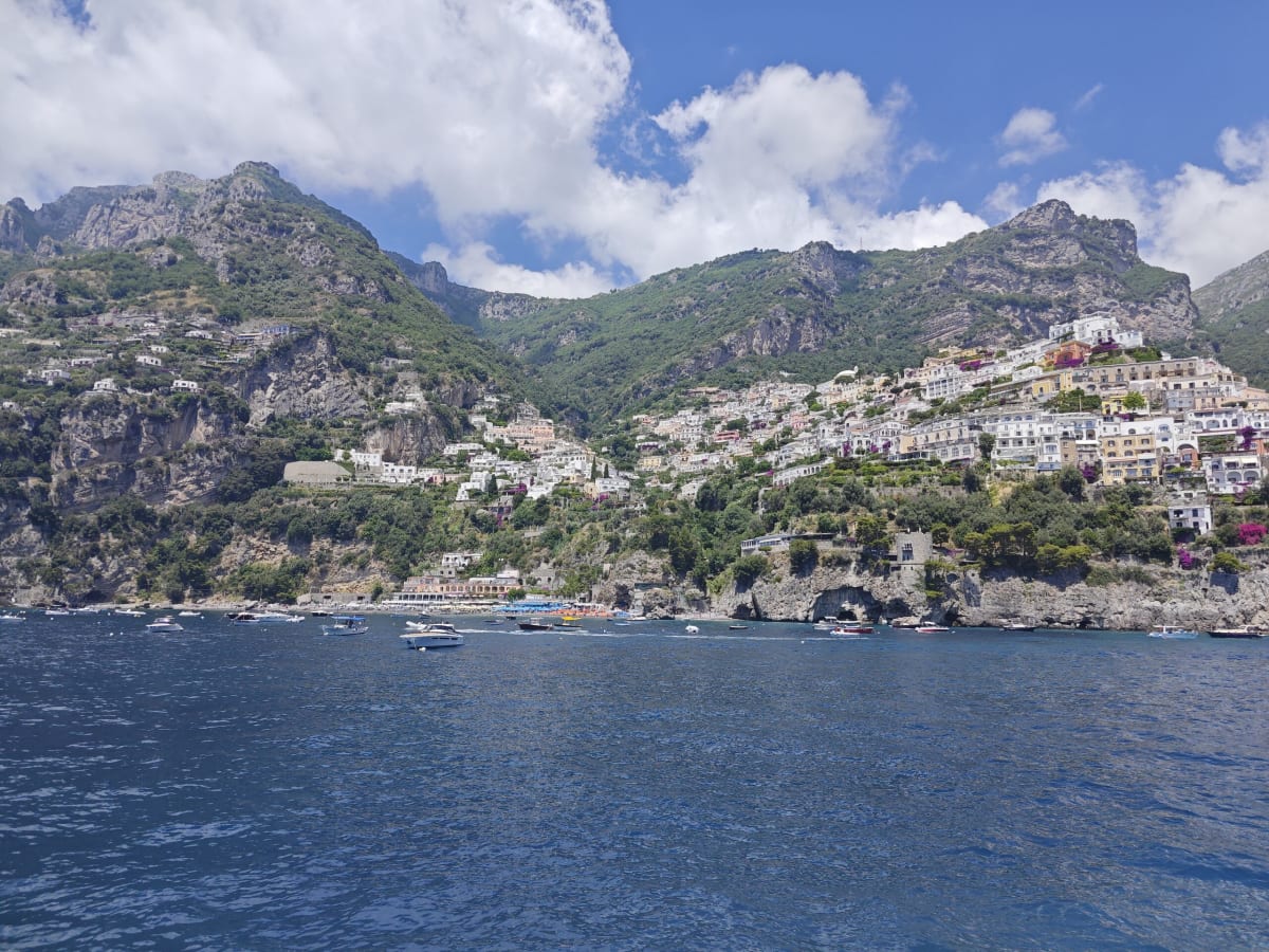 A wide view across the Amalfi coast with clusters of white and pale houses running along the hillside above the blue sea