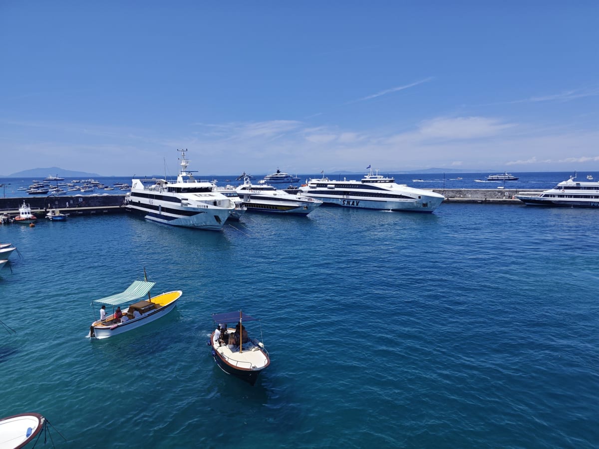 Motor boats and yachts on deep blue water off Capri's harbour, a line of large white yachts lying along the mole