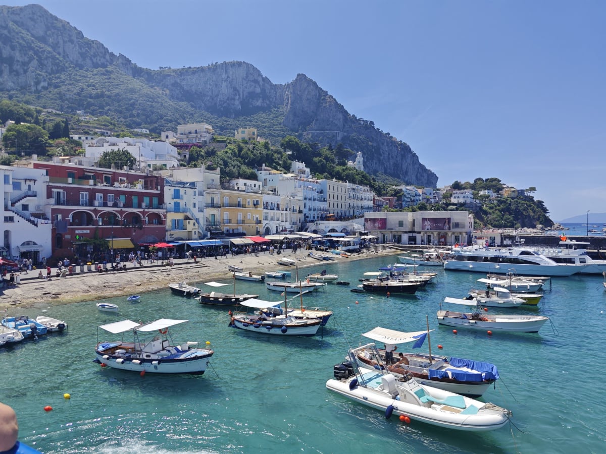 Small wooden boats and a rigid inflatable in the green shallows of Capri's harbour beside the beach and its row of pastel houses