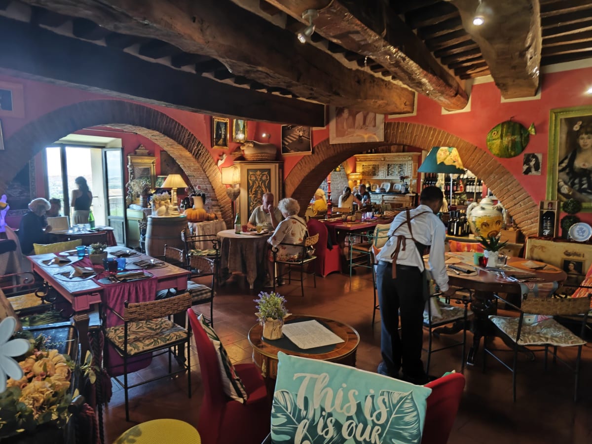 A warm, cluttered trattoria with arched alcoves painted red, timber ceiling beams and a waiter moving between the tables