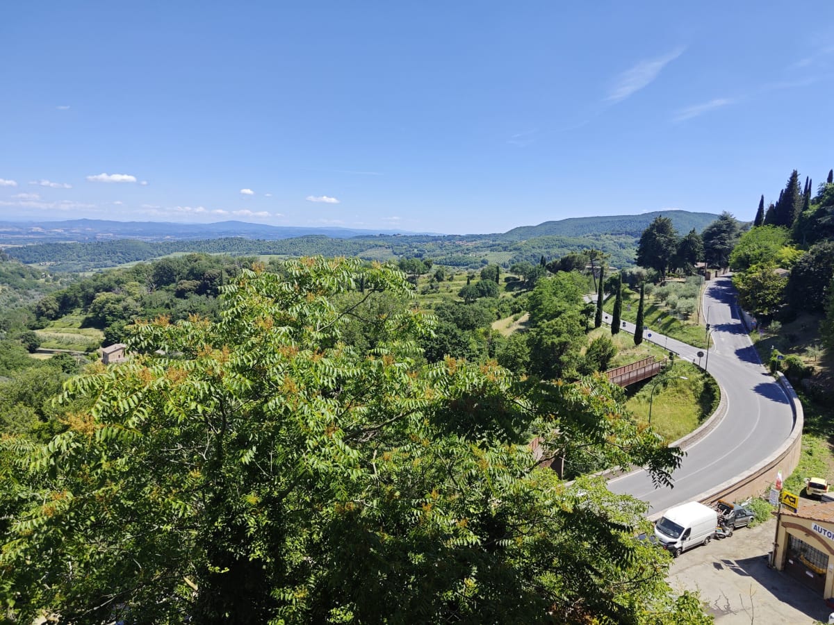 A view from the hilltop over green Tuscan countryside, a road curving down through cypresses and the hazy plain beyond