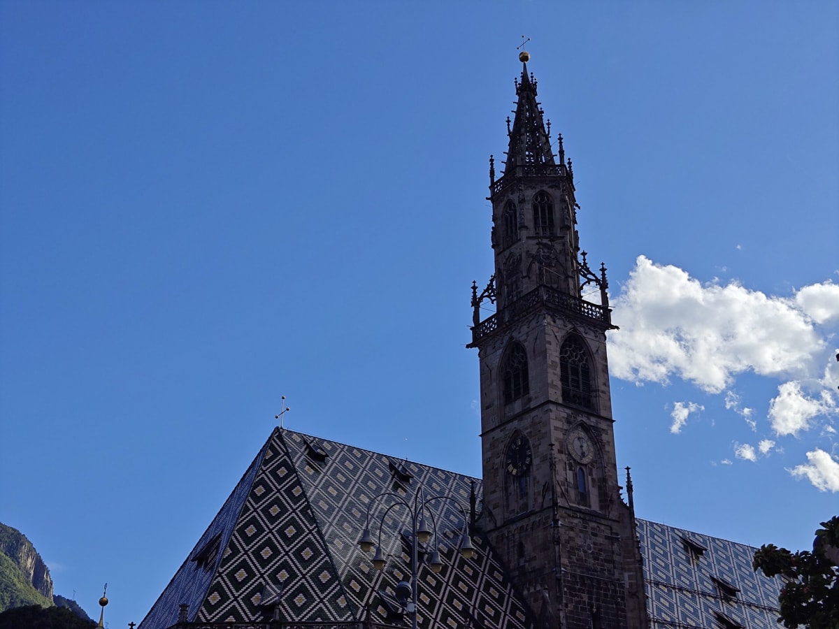 Bolzano Cathedral — the openwork Gothic bell tower and the diamond-patterned glazed-tile roof against a blue sky