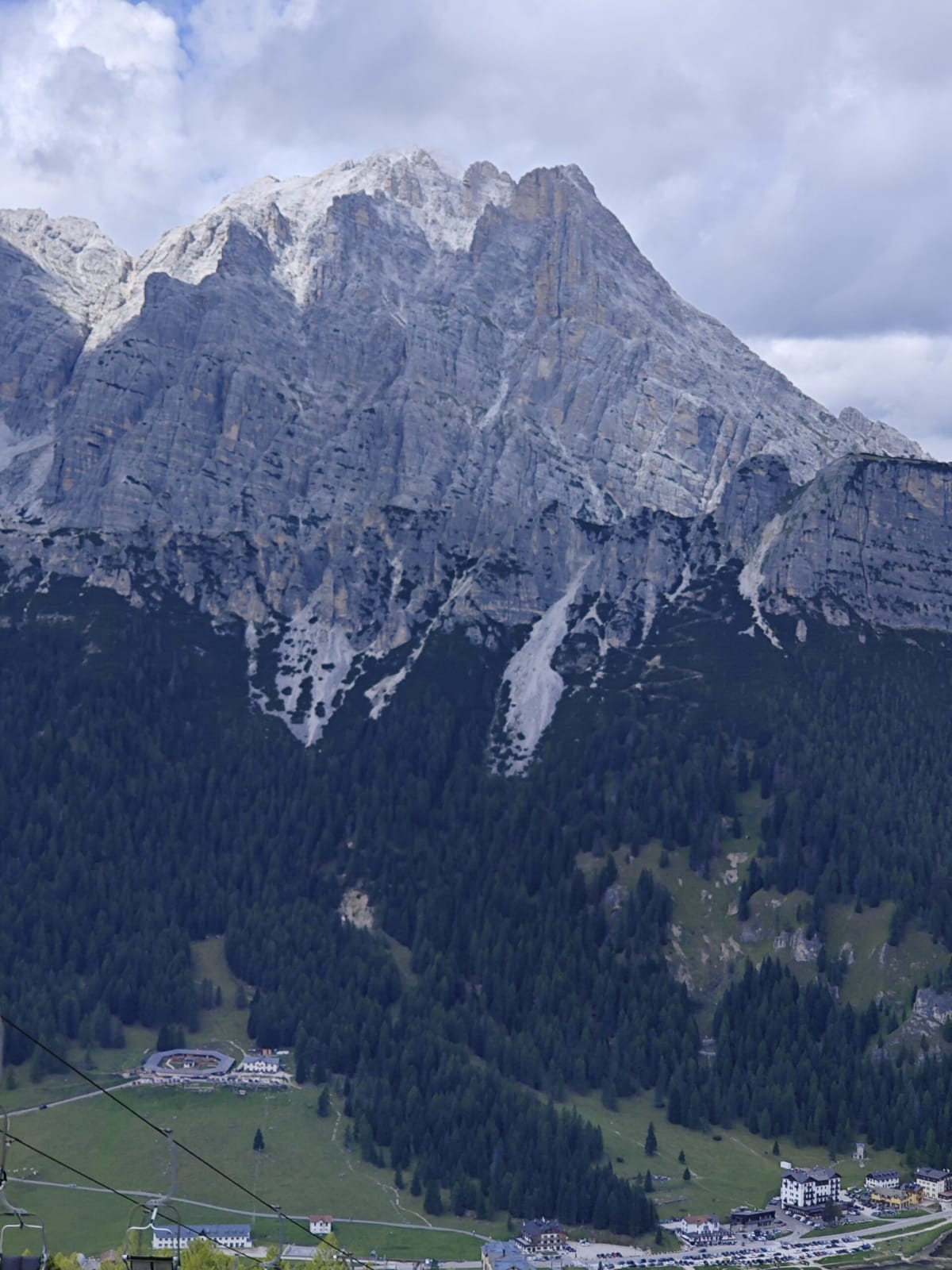 A vast grey Dolomite wall of the Sorapiss group seen from a chairlift, cables crossing the frame, the valley far below