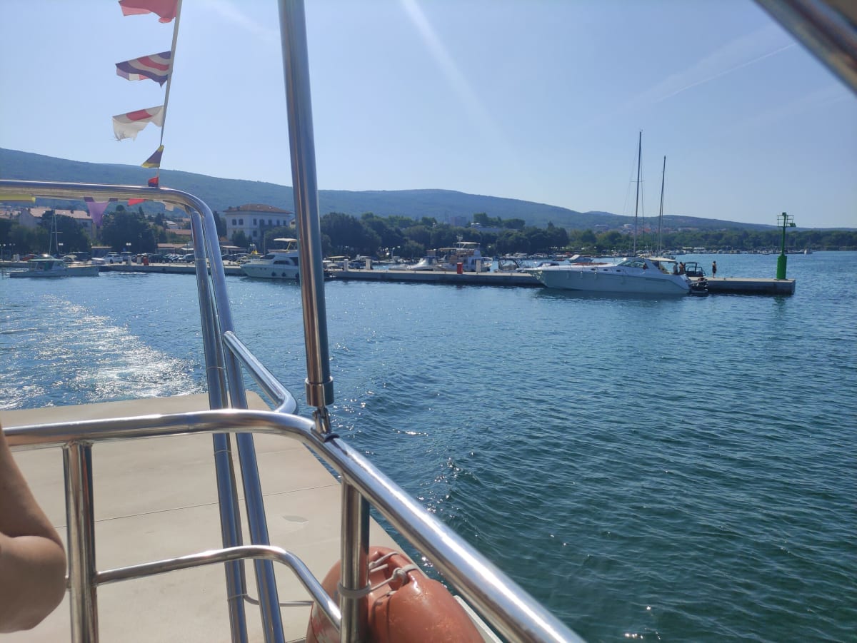 Punat's marina and waterfront seen from a boat decked with dazzle bunting, the wooded ridge of Krk rising behind