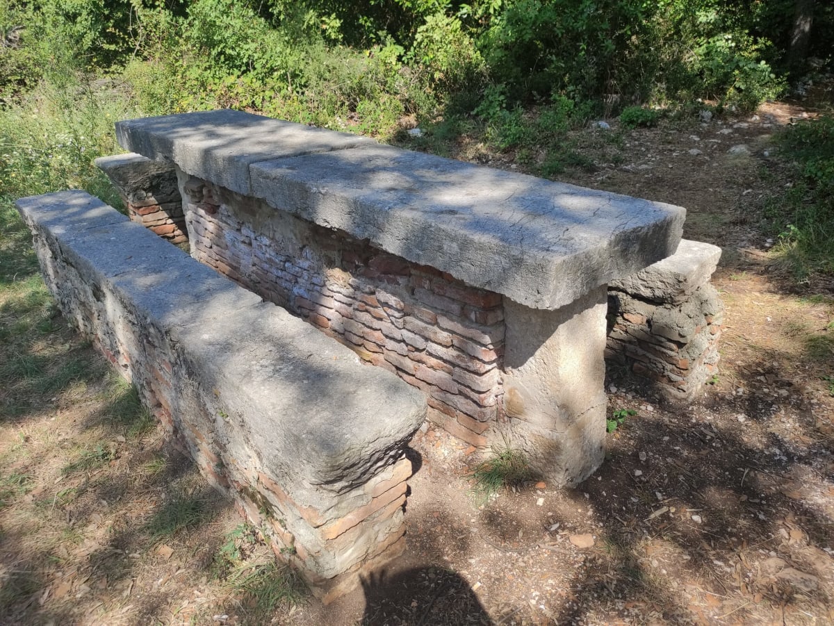 A weathered old stone-and-brick table with matching benches standing in a clearing in the woods on Košljun