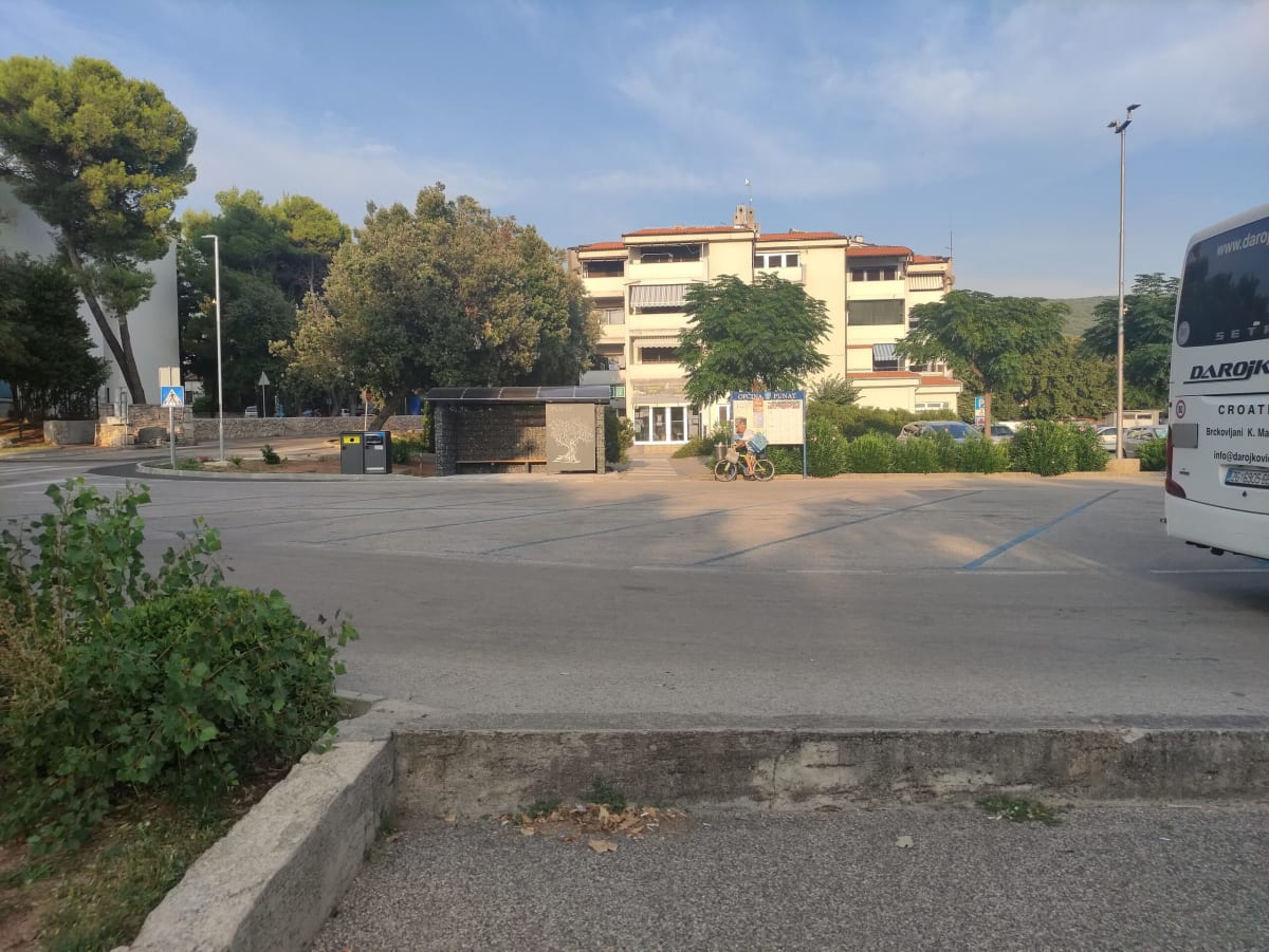 The end of the day back in Punat — a near-empty coach park by the municipal building and tourist office, a "Punat" sign with an olive-tree logo