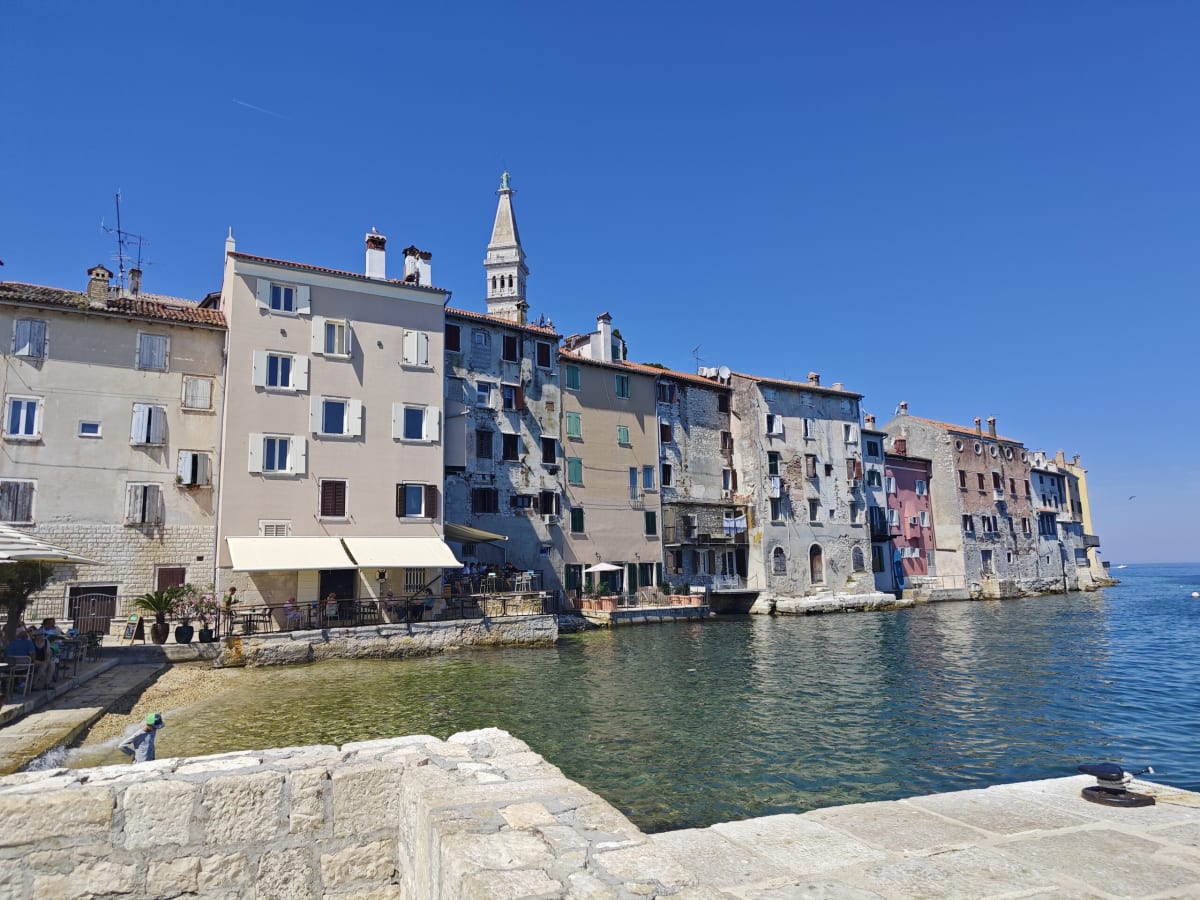 Tall weathered houses rising straight from the water at the edge of Rovinj's old town, the slender campanile of St Euphemia behind and a stone mole in the foreground