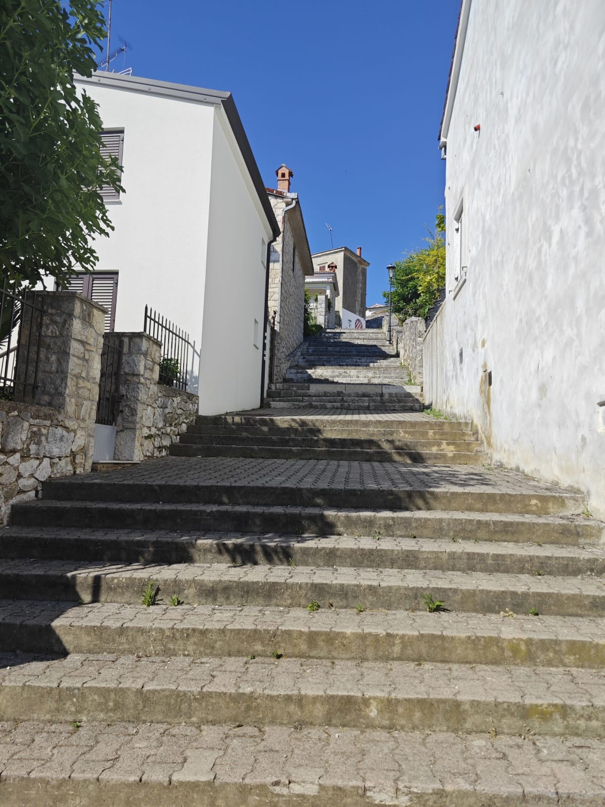 A steep stone stairway climbing between whitewashed walls under a bright blue sky