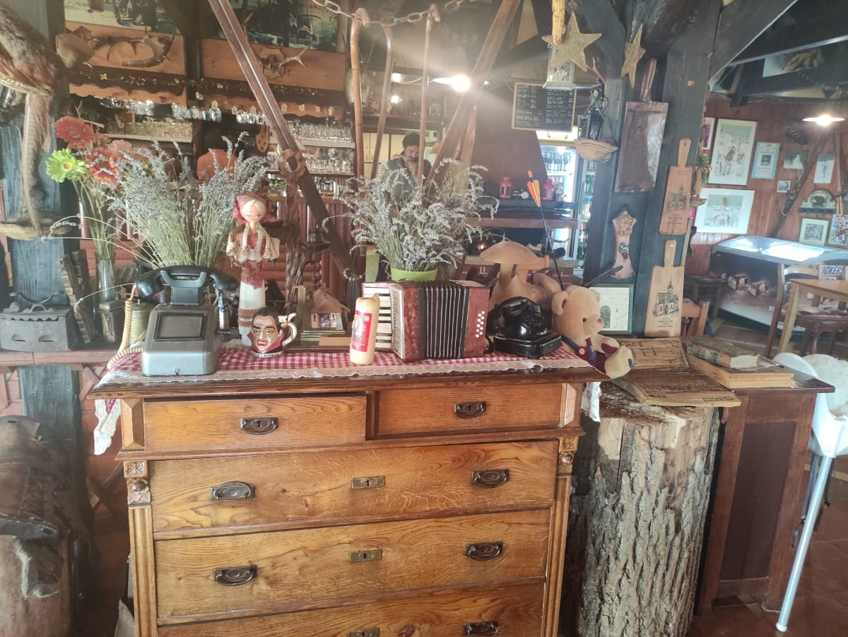 An antique oak chest of drawers in the lodge crowded with bric-a-brac — two rotary telephones, a costumed folk doll, an accordion, dried flowers and a teddy bear