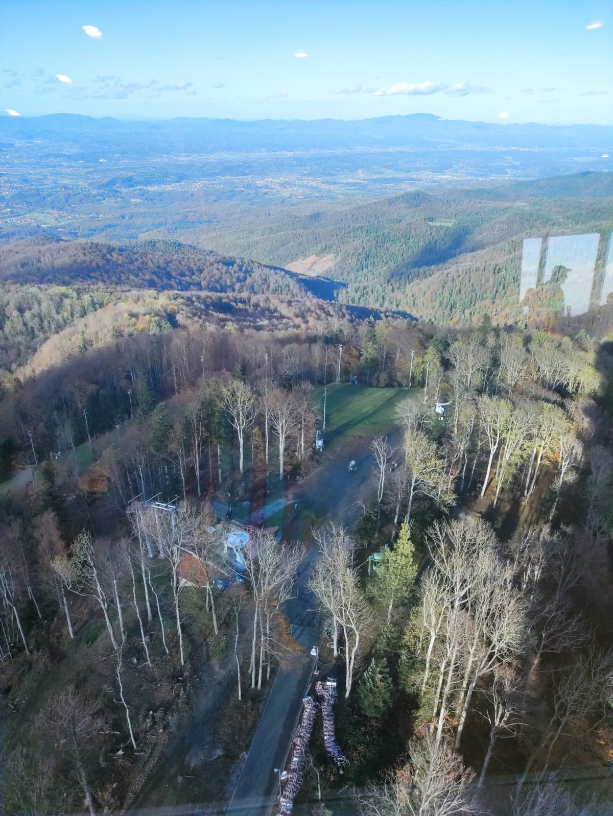 Looking down from the tower onto the top-station area — the ski-piste clearing, chairlift line and racks of stacked rental gear among the trees