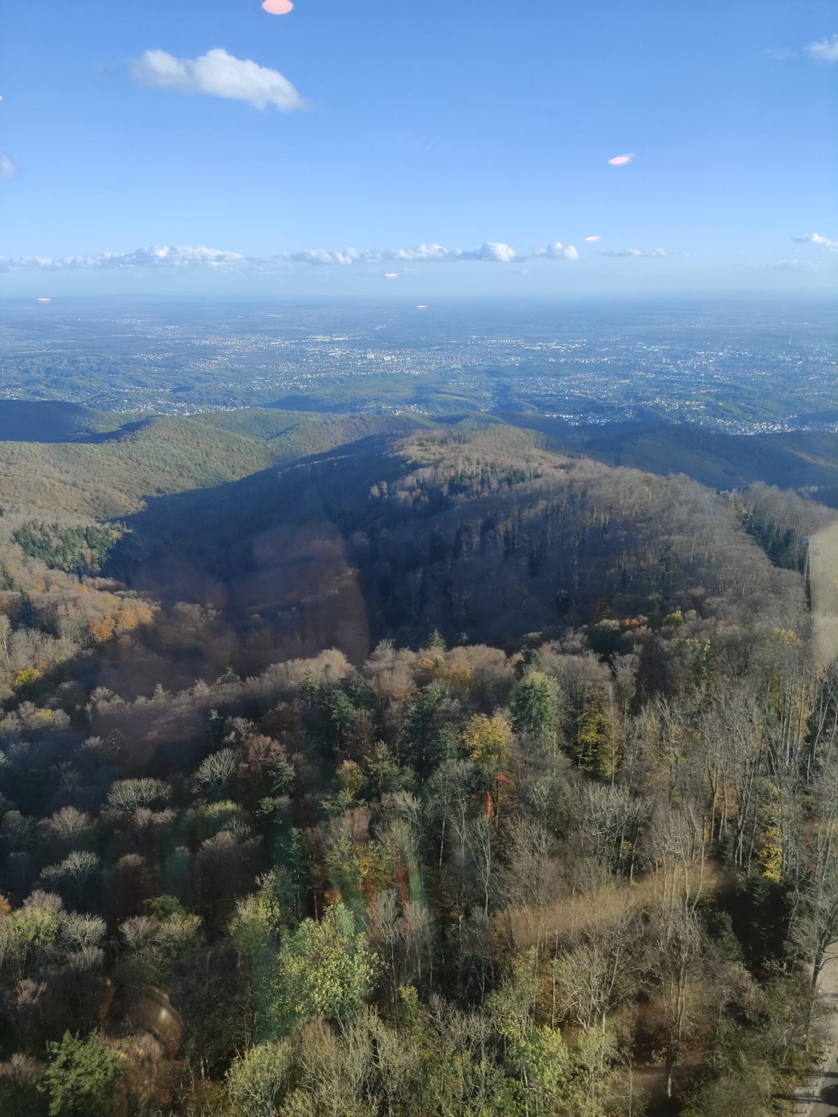 Wooded Medvednica ridges rolling down toward Zagreb and the hazy plain, low afternoon light picking out the autumn colour, shot through the tower glass