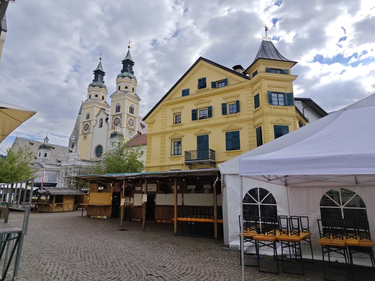 A yellow Baroque house in front of the cathedral's twin towers in Brixen, beer tents and benches set out along the street