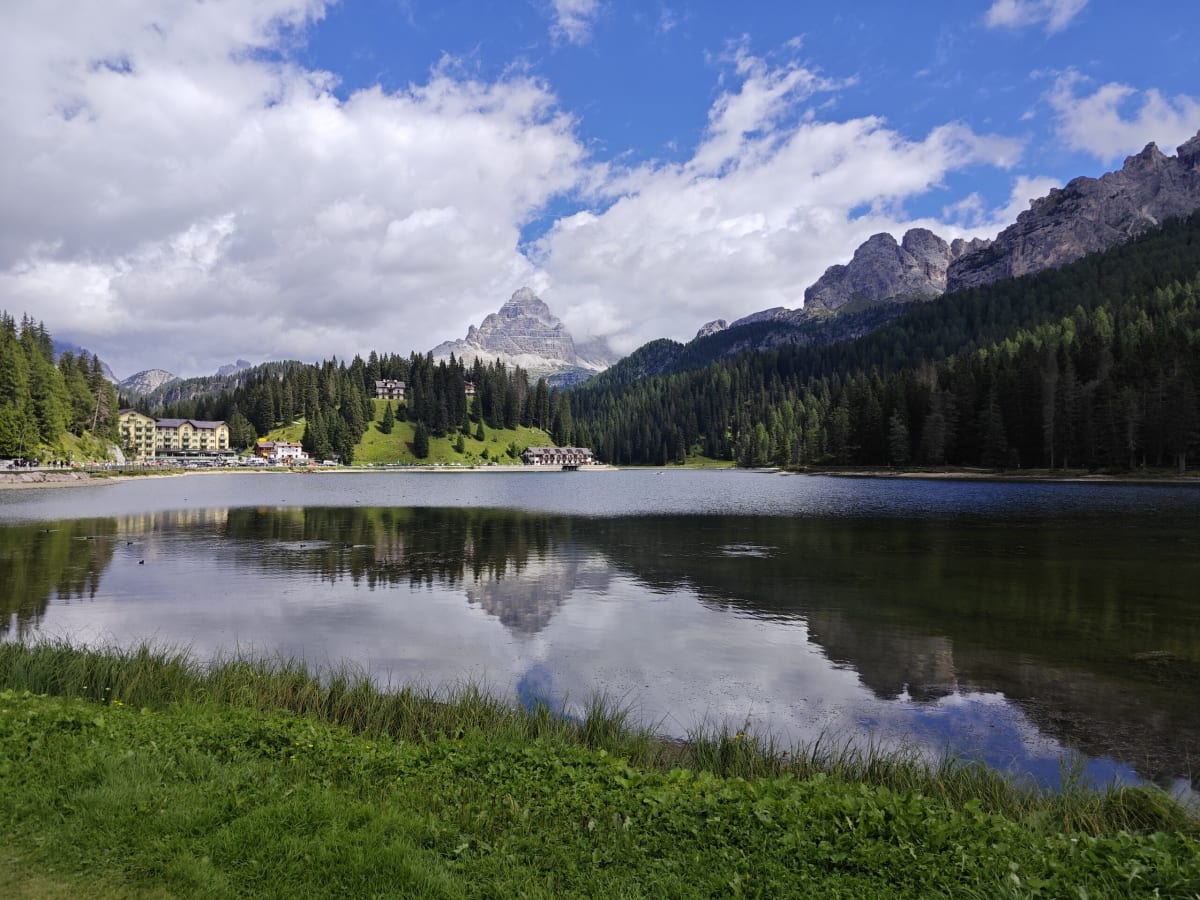 Lago di Misurina, its still water reflecting clouds and dark forest, the Dolomite peaks of the Cadini behind the shoreline