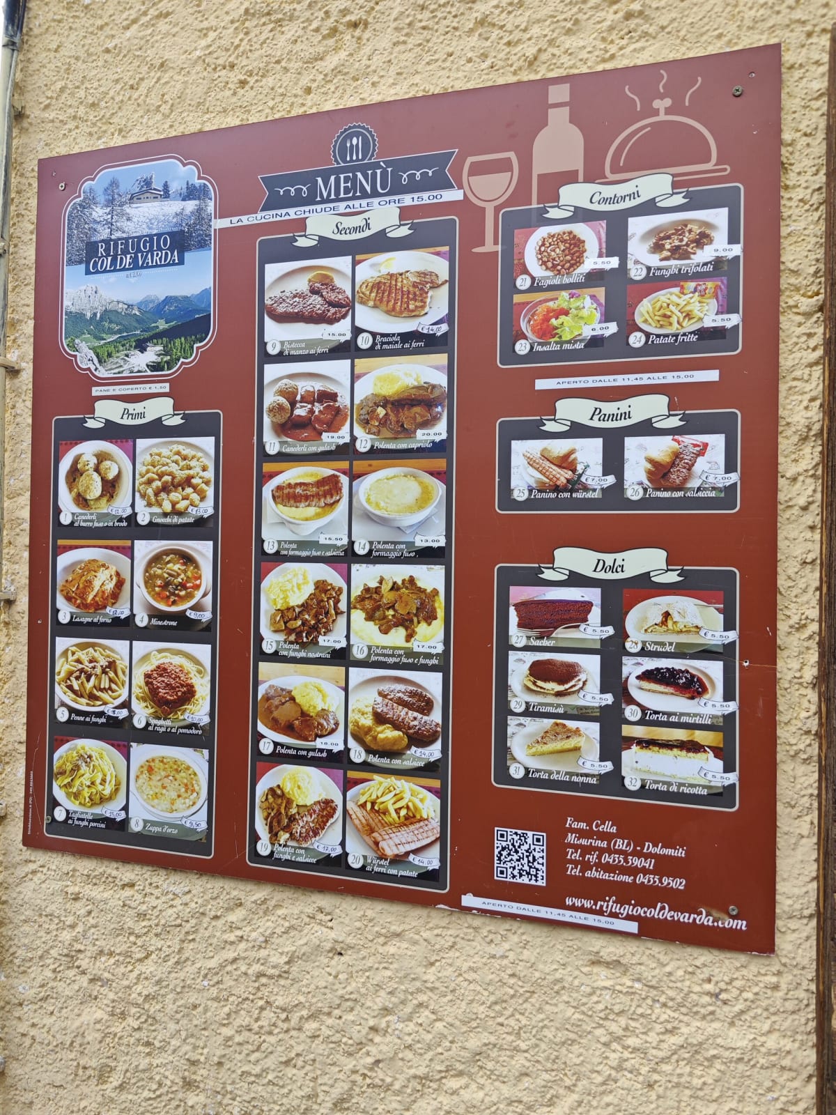 A rifugio's illustrated menu board on a cream-coloured wall, photos of dishes arranged by course