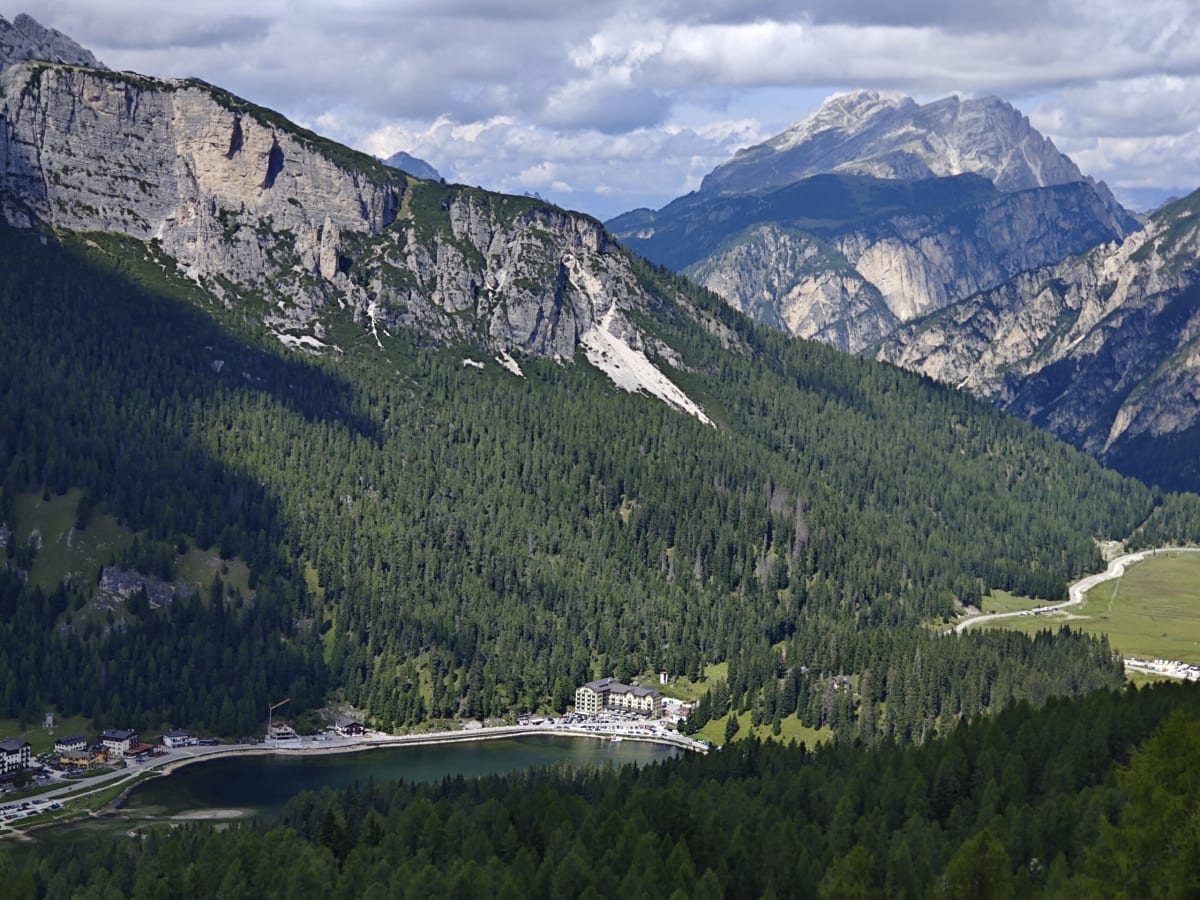Looking down on Lago di Misurina from a mountain above, the lake cradled by forested slopes and an alpine meadow beyond