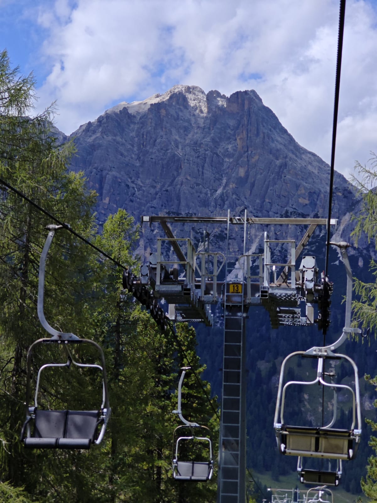 Empty chairlift seats and a pylon rising up the mountainside, a Dolomite summit looming behind