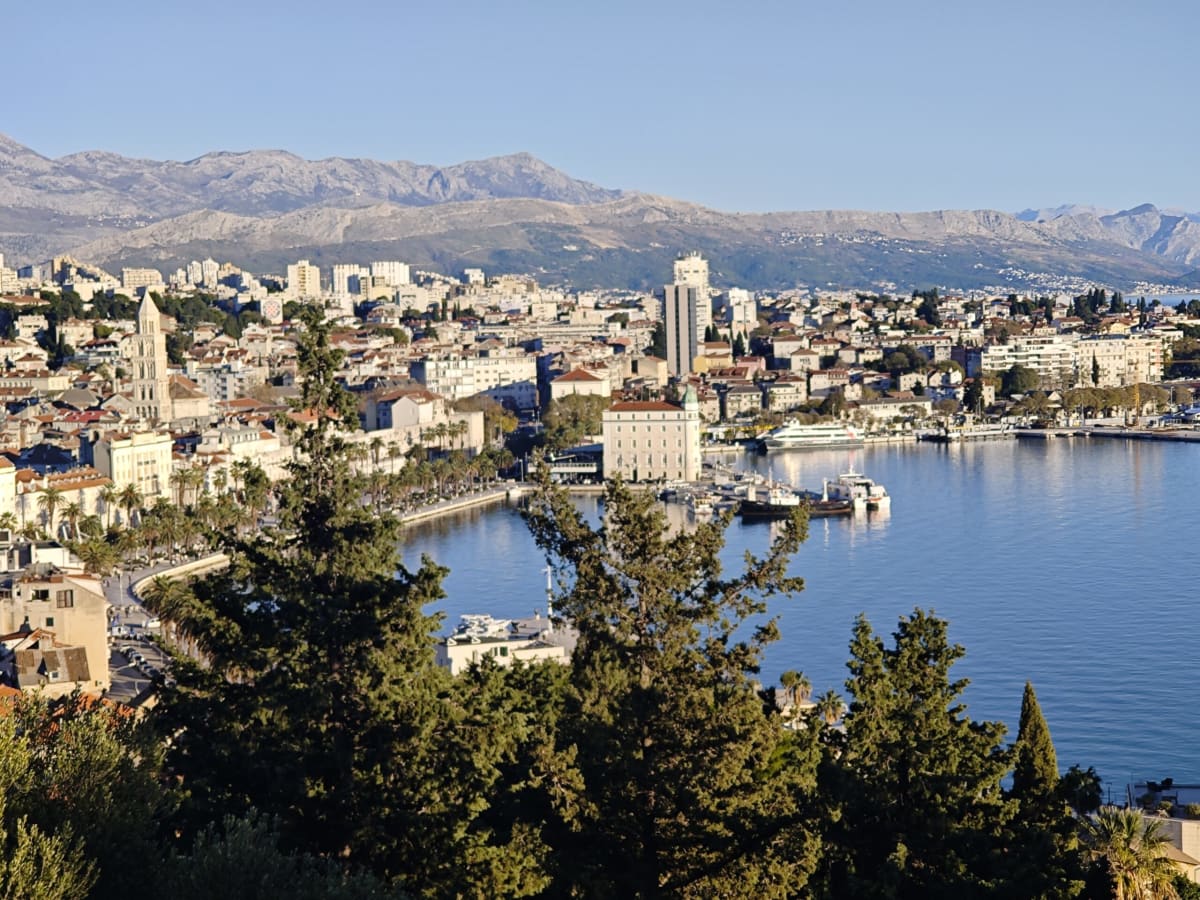 Split seen from the slopes of Marjan — the old town and its Romanesque cathedral campanile on the left, the harbour and ferry quay on the right, with the bare grey ridge of Mosor filling the horizon