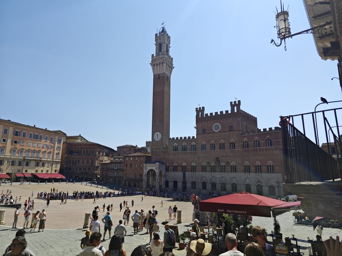 Piazza del Campo in Siena — the shell-shaped square filled with people and the tall brick Torre del Mangia beside the crenellated Palazzo Pubblico
