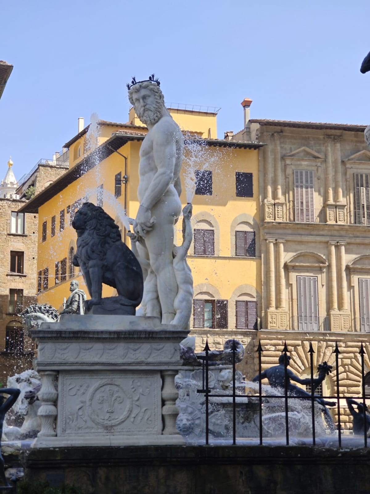 The bronze Neptune on the fountain in Piazza della Signoria, a lion statue at its side and yellow palazzi behind
