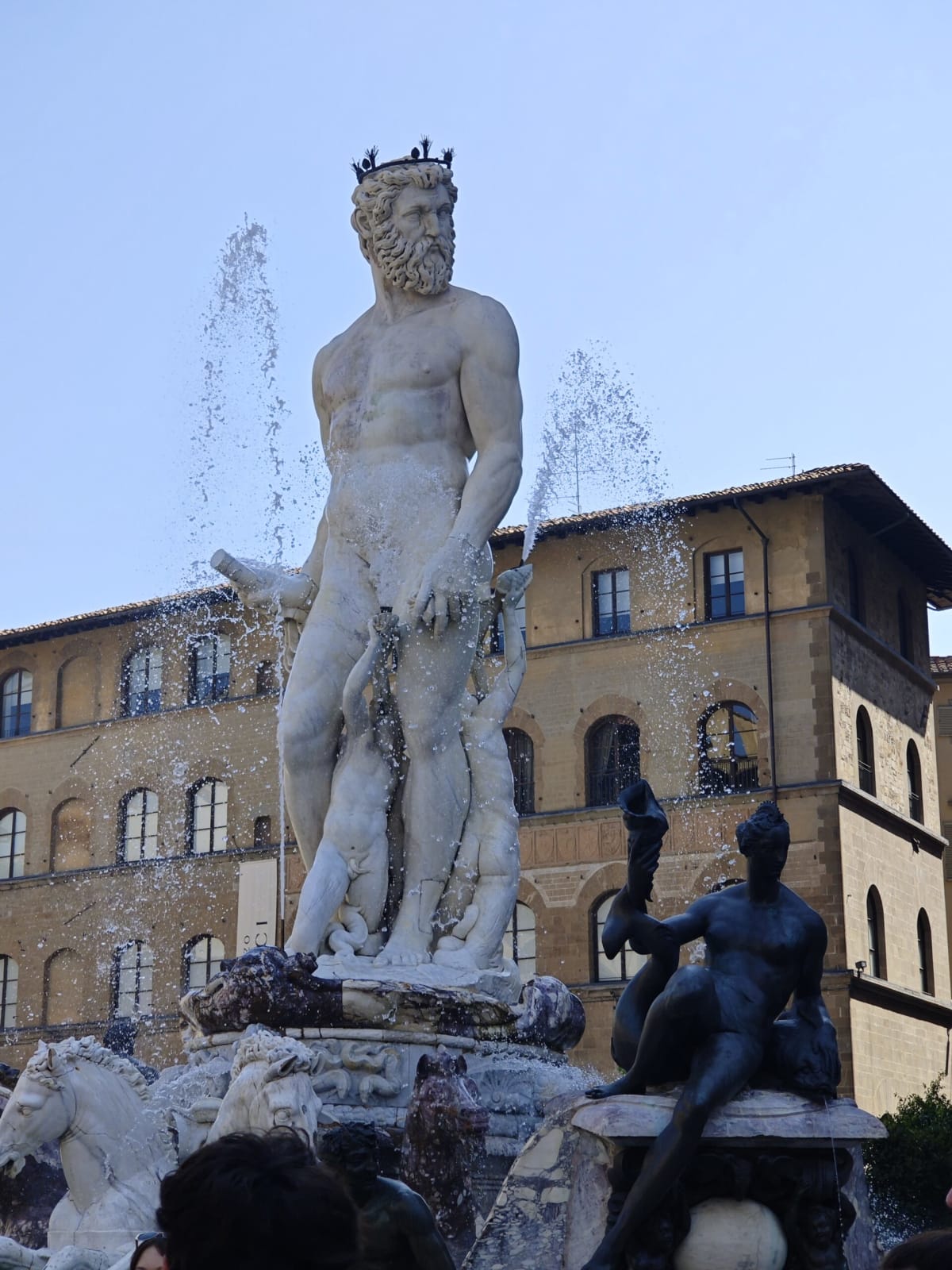Neptune and his horses on the Fountain of Neptune, water arcing through the sun against a clear sky