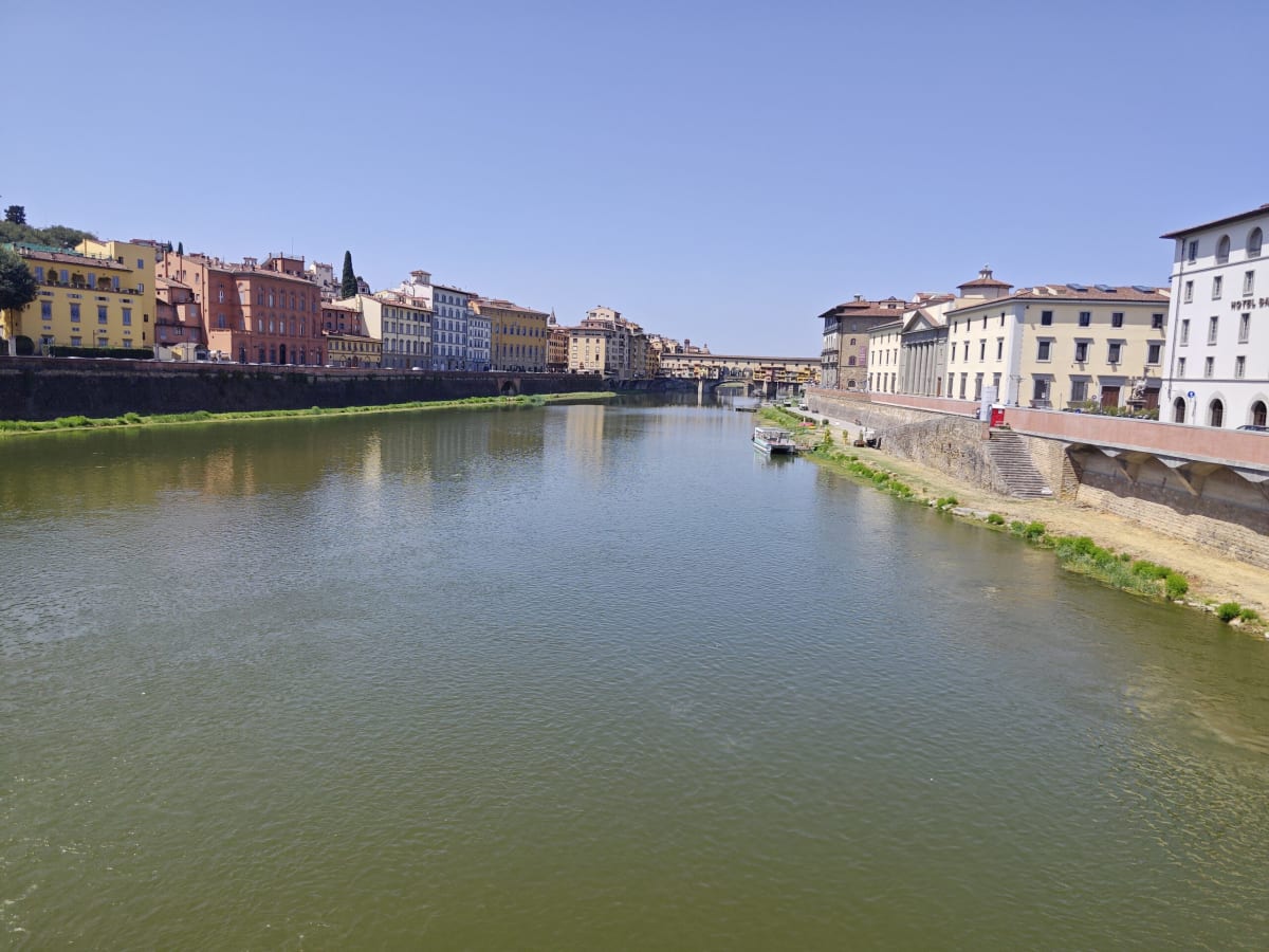 The Arno at Florence, green water between low pastel houses along the bank, the Ponte Vecchio distant in the haze