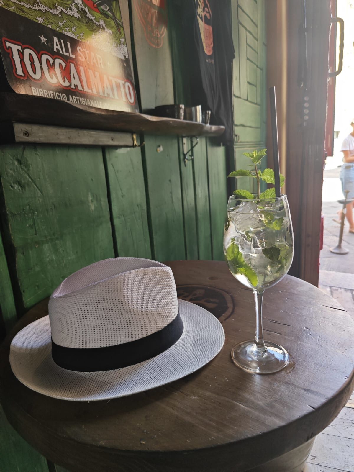 A cold drink in a tall glass with a sprig of mint on a barrel table at a bar, a white straw hat with a black band beside it