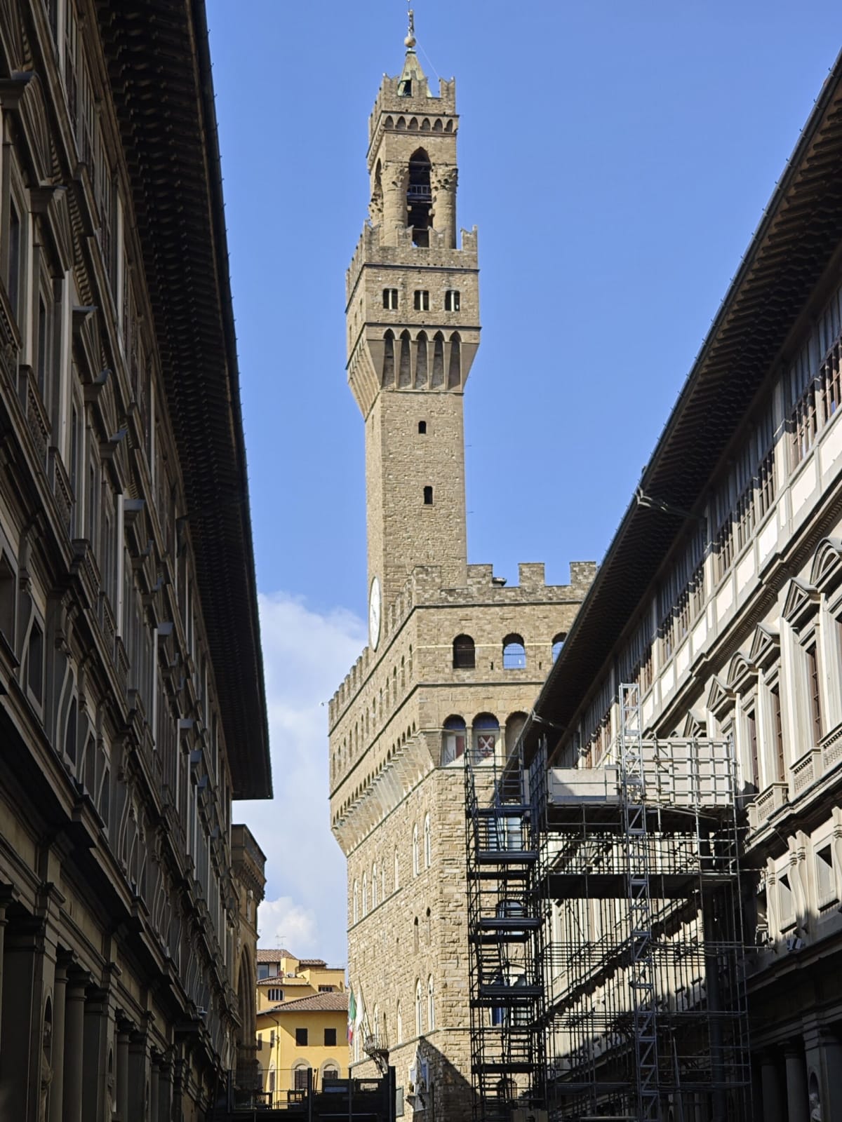 Palazzo Vecchio's tower between the long walls of the Uffizi, scaffolding on the corner building and a thin streak of cloud above