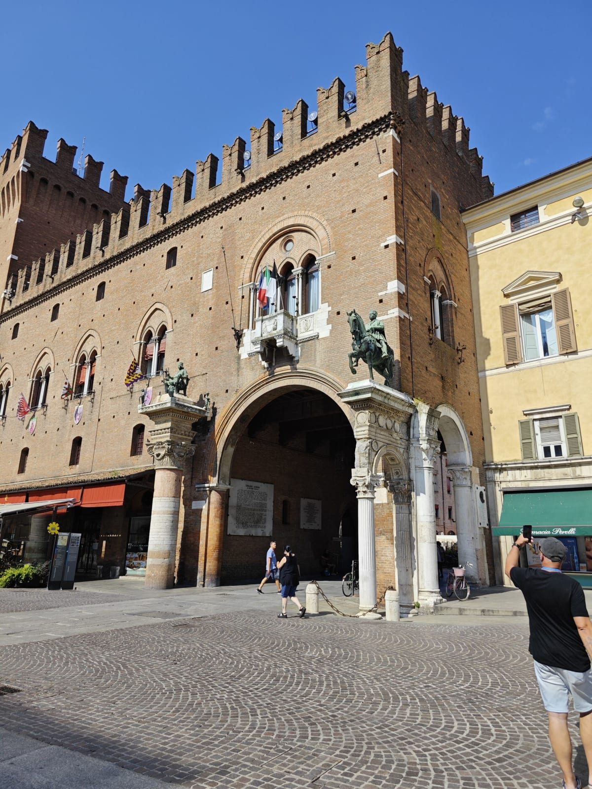 The Palazzo Municipale in Ferrara — a crenellated brick façade over a stone archway with equestrian statues on its columns