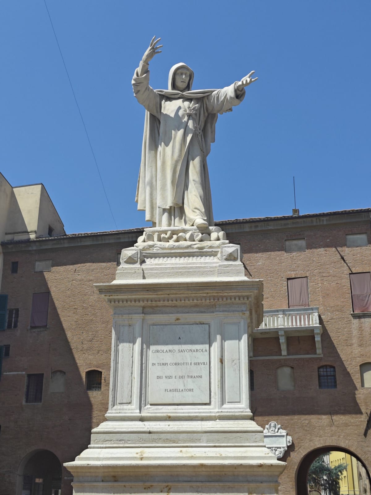 The white marble statue of Savonarola on a high plinth, arms outstretched, in front of a brick palazzo