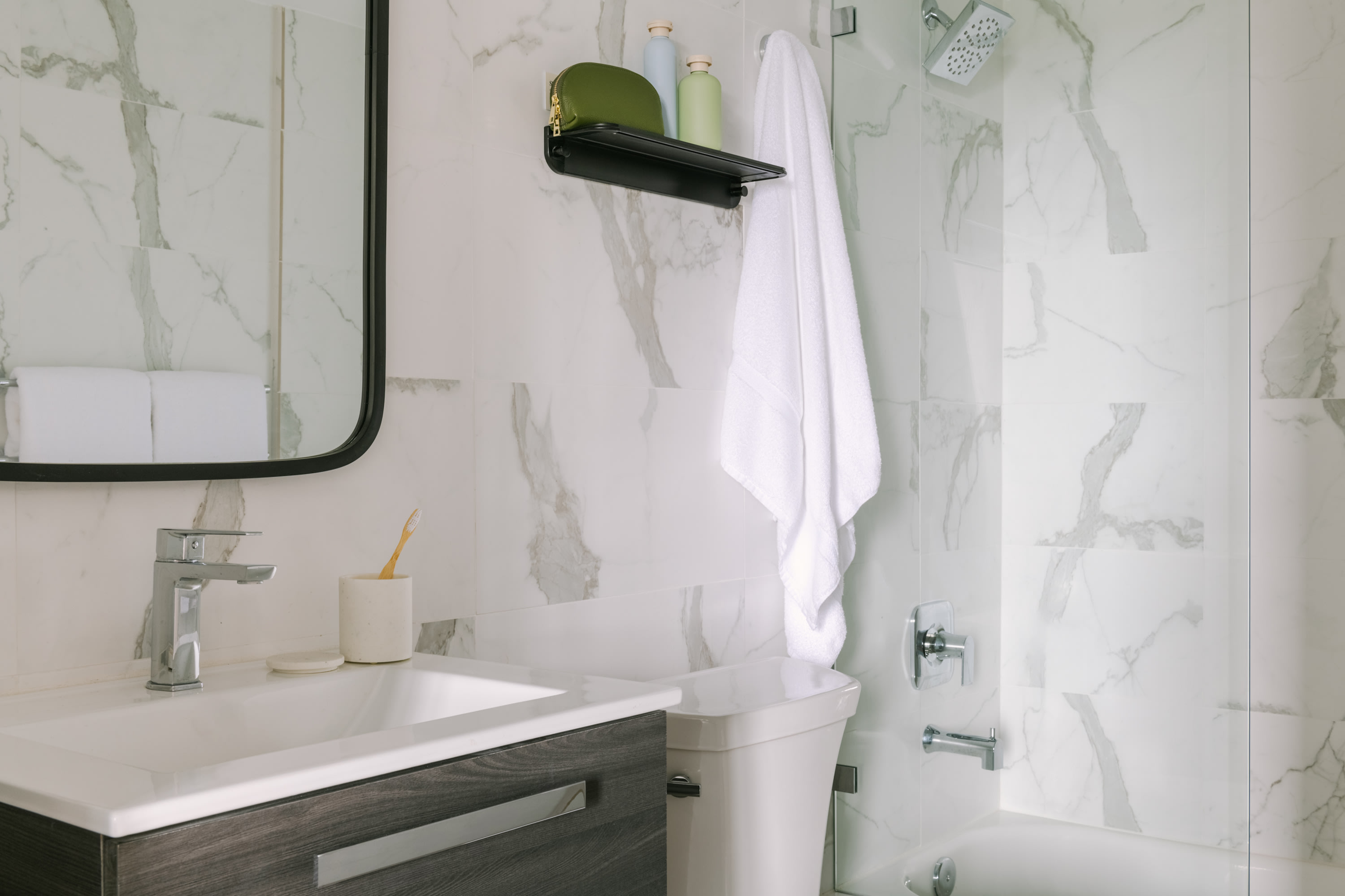 A white sink and dark wood vanity sit in the foreground of a bathroom with white marble walls and a shower area in the background.