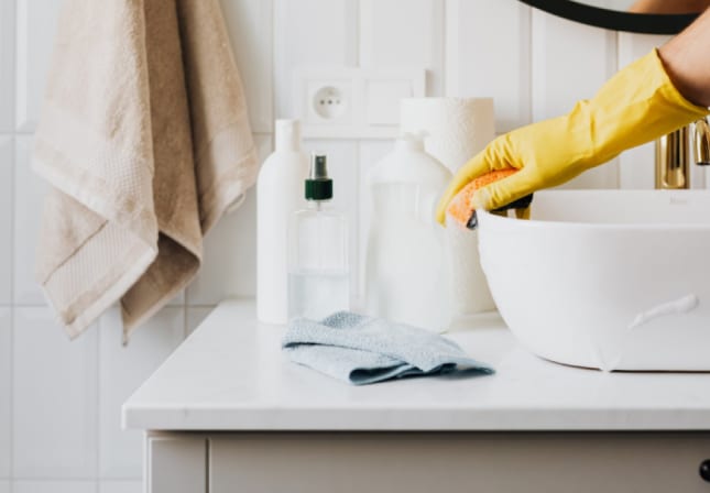 A Kasa housekeeper cleaning a bathroom sink.