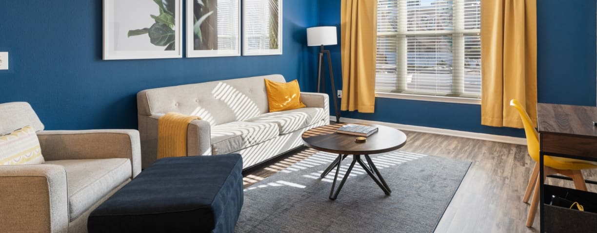 A bright living room with blue and yellow tints featuring a queen sized beige sofa with a matching armchair.