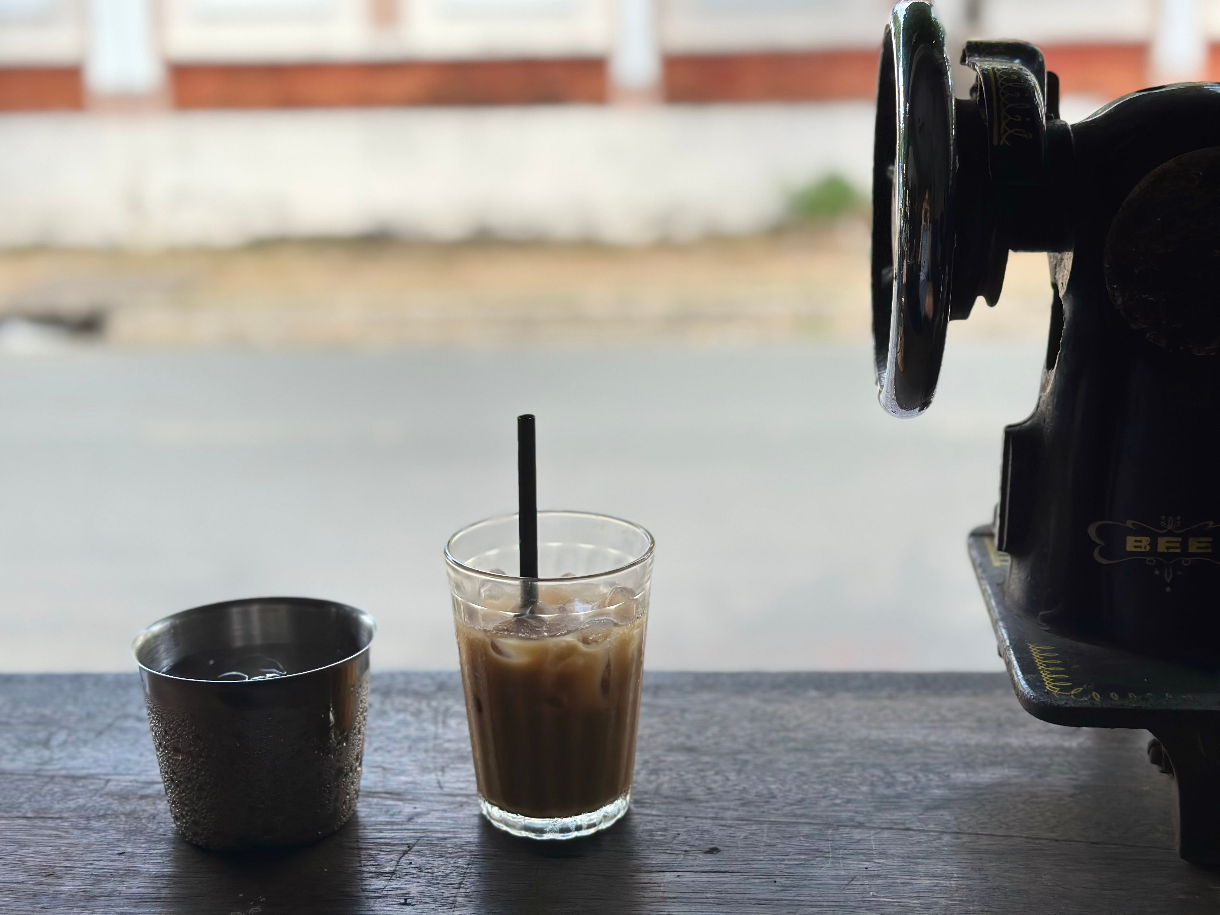 Ly cà phê sữa đá, cạnh ly nước đá và chiếc máy may cũ