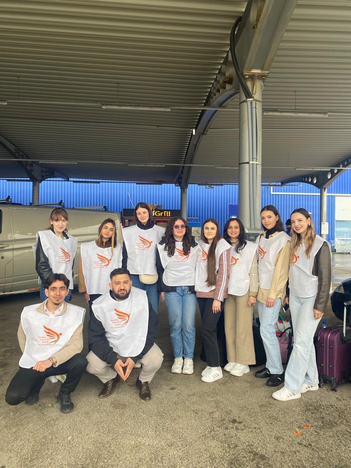 Un grup de voluntari tineri, în vestele albe cu sigla asociației, într-o sală din tabără
