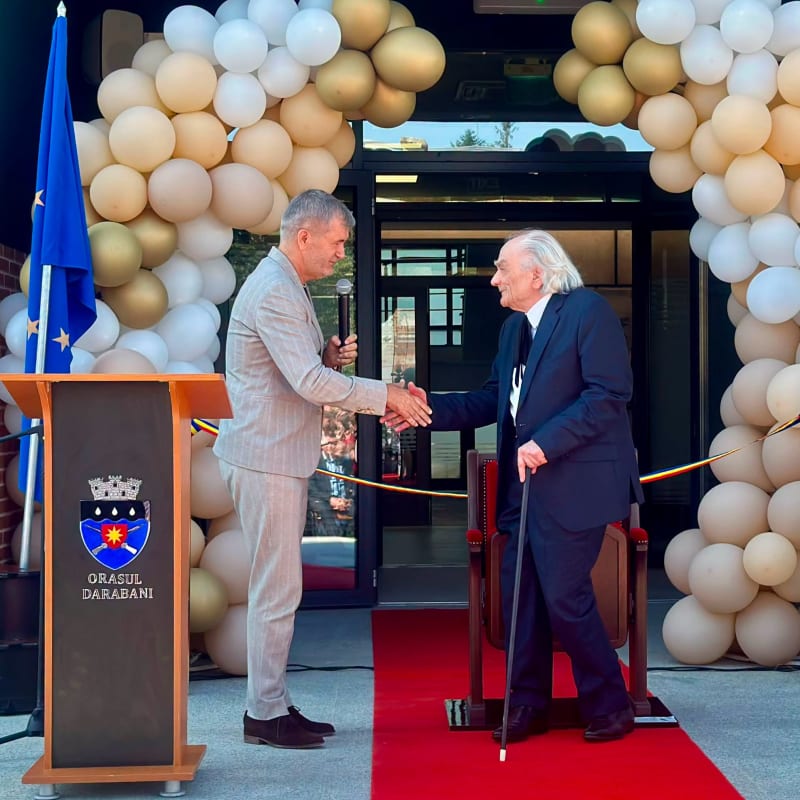 Valeriu Iftime dând mâna cu un invitat la o inaugurare, sub o arcadă de baloane