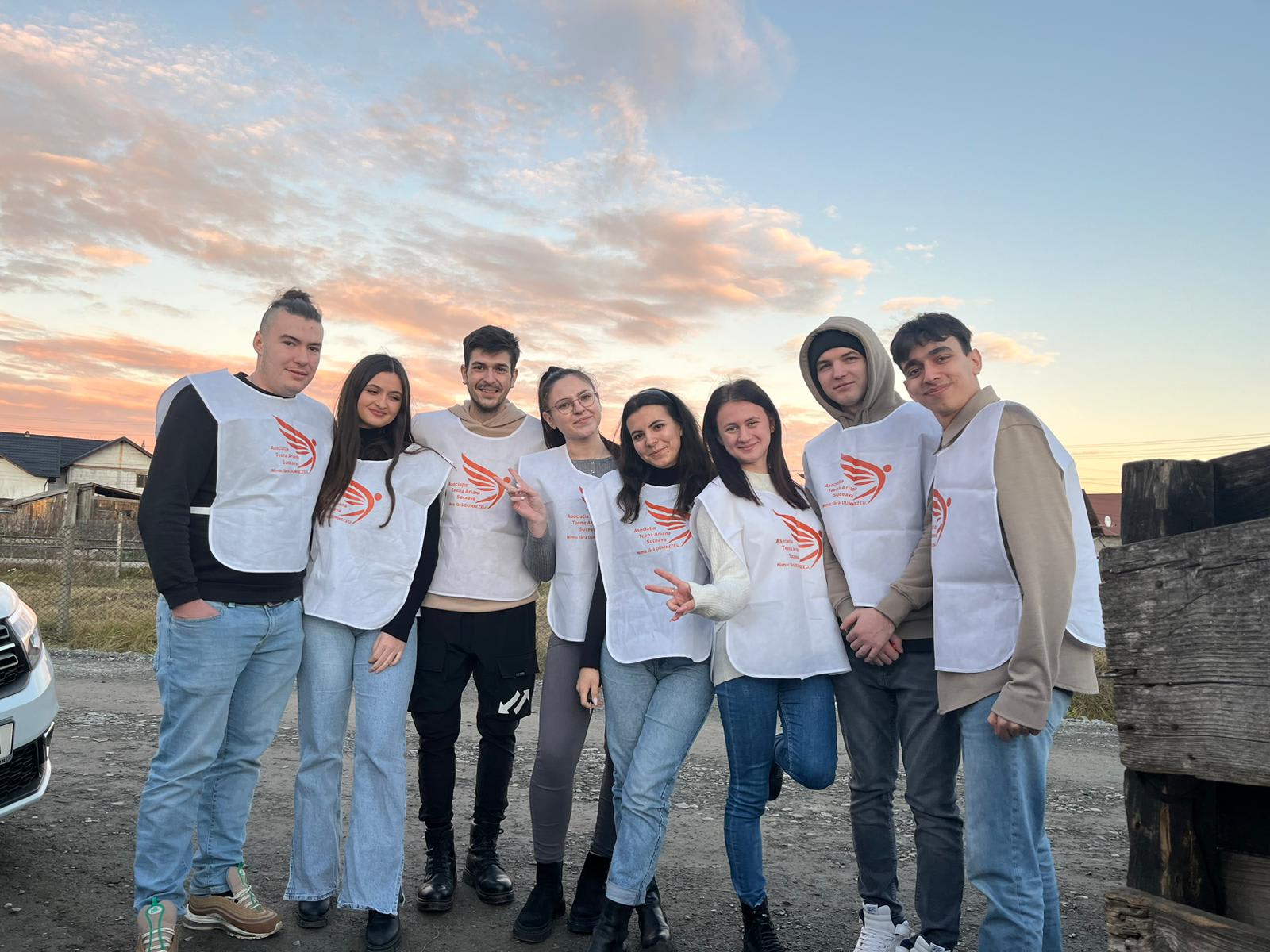 Opt voluntari tineri, în veste albe cu sigla asociației, în grup, la apus